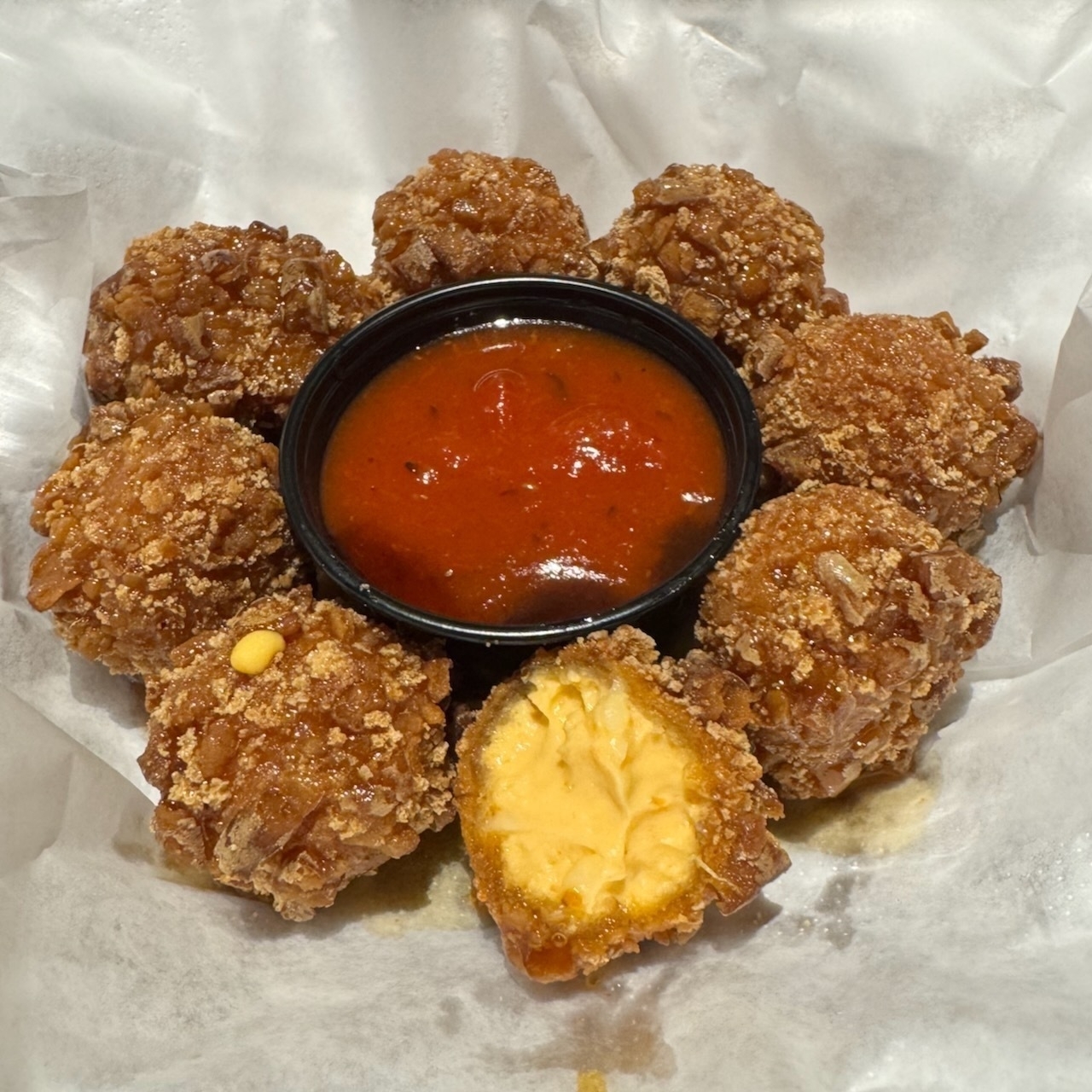 Auto-generated description: Fried mac and cheese balls arranged around a container of red dipping sauce.